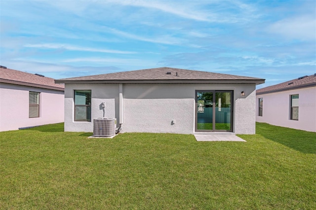 back of house with a yard, roof with shingles, stucco siding, and central AC