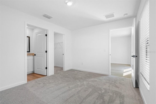 unfurnished bedroom featuring baseboards, connected bathroom, carpet floors, a walk in closet, and visible vents
