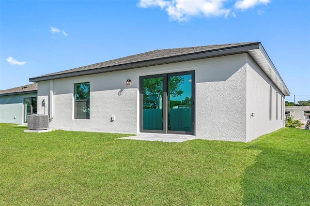 rear view of house featuring cooling unit, a lawn, and stucco siding