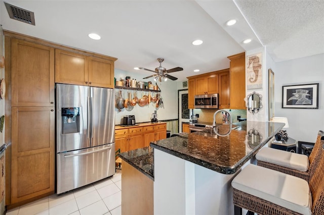 kitchen featuring visible vents, appliances with stainless steel finishes, a peninsula, brown cabinets, and dark stone counters