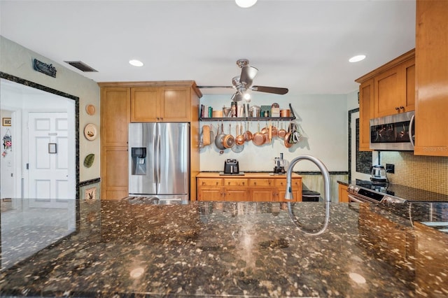 kitchen featuring dark stone countertops, visible vents, decorative backsplash, stainless steel appliances, and ceiling fan