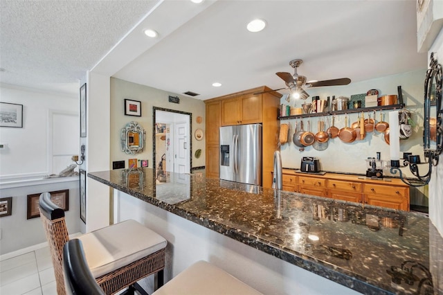kitchen featuring light tile patterned floors, stainless steel refrigerator with ice dispenser, a ceiling fan, recessed lighting, and dark stone counters