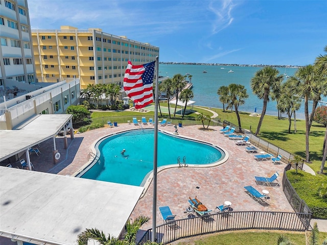 pool featuring a water view, fence, a patio, and a lawn