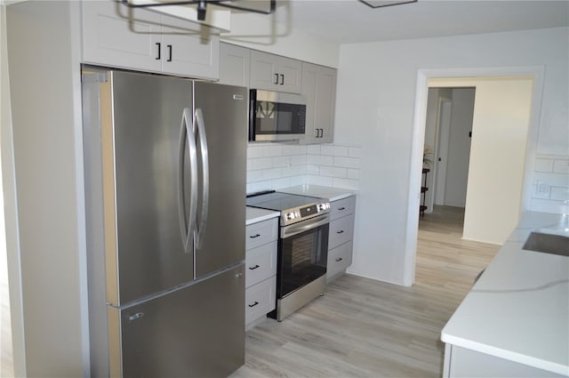 kitchen with tasteful backsplash, gray cabinets, light countertops, appliances with stainless steel finishes, and light wood finished floors
