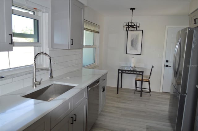 kitchen with hanging light fixtures, a sink, light wood finished floors, stainless steel appliances, and light stone counters