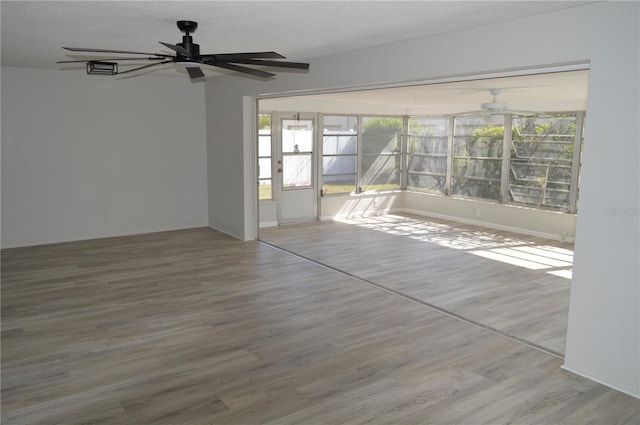empty room featuring wood finished floors, baseboards, and a ceiling fan