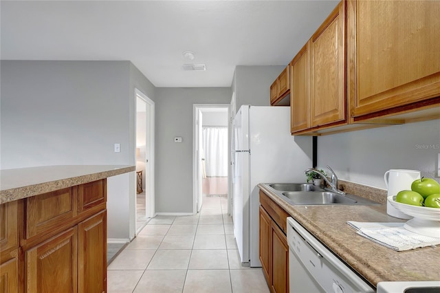 kitchen featuring a sink, light tile patterned floors, white appliances, and brown cabinets