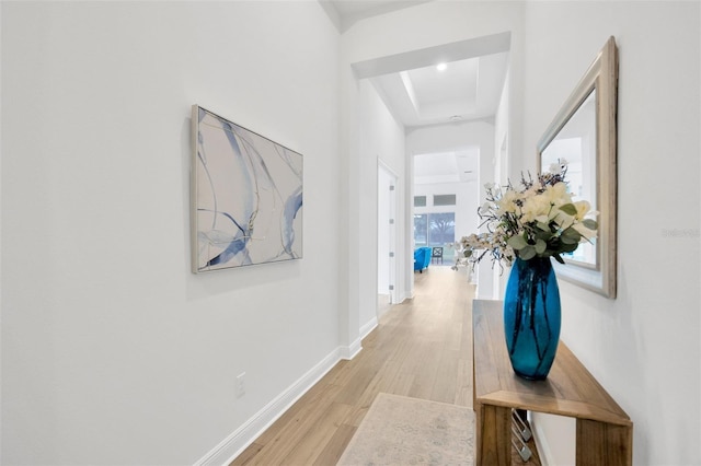 corridor featuring a raised ceiling, light wood-style floors, and baseboards