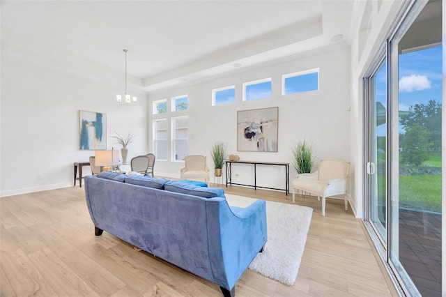 living room with a tray ceiling, light wood-type flooring, a notable chandelier, and baseboards