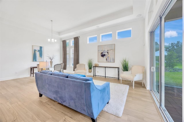 living room with a chandelier, a tray ceiling, baseboards, and light wood-style flooring