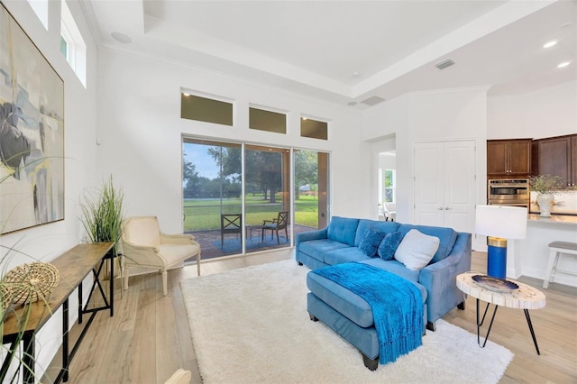 living area with a raised ceiling, light wood-style floors, crown molding, and visible vents