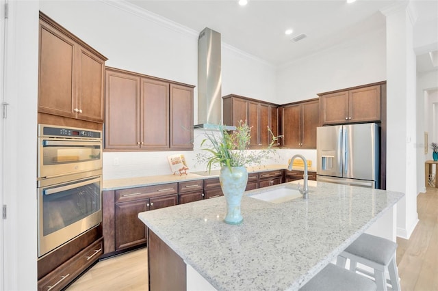 kitchen with ornamental molding, light wood-style flooring, wall chimney exhaust hood, appliances with stainless steel finishes, and a sink