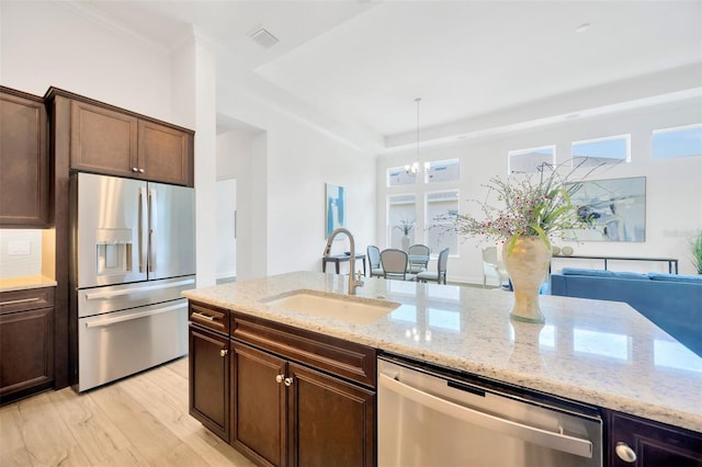 kitchen featuring a notable chandelier, a sink, appliances with stainless steel finishes, dark brown cabinetry, and light wood-style flooring