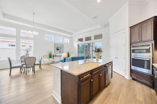 kitchen with a sink, a tray ceiling, appliances with stainless steel finishes, and light wood-style floors