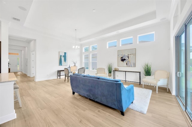 living room with visible vents, a raised ceiling, a chandelier, and light wood-style floors