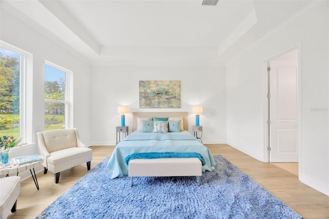 bedroom with visible vents, baseboards, ornamental molding, a tray ceiling, and light wood-style flooring