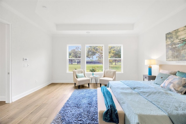 bedroom featuring crown molding, a tray ceiling, baseboards, and wood finished floors