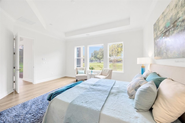 bedroom with a raised ceiling, visible vents, baseboards, and wood finished floors