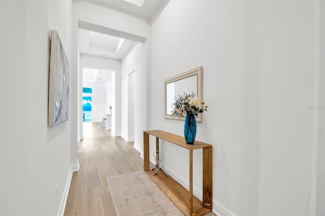 corridor featuring baseboards, light wood-type flooring, and a raised ceiling