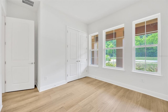 unfurnished bedroom with light wood-style floors, visible vents, baseboards, and a closet
