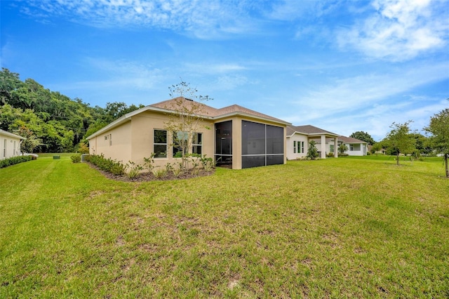 rear view of property with a yard, a sunroom, and stucco siding