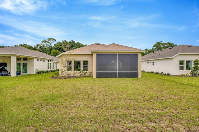 back of house featuring stucco siding, a sunroom, and a lawn