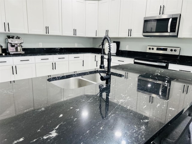 kitchen with white cabinetry, stainless steel appliances, dark stone countertops, and a sink