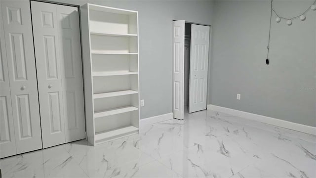 unfurnished bedroom with two closets, marble finish floor, and baseboards