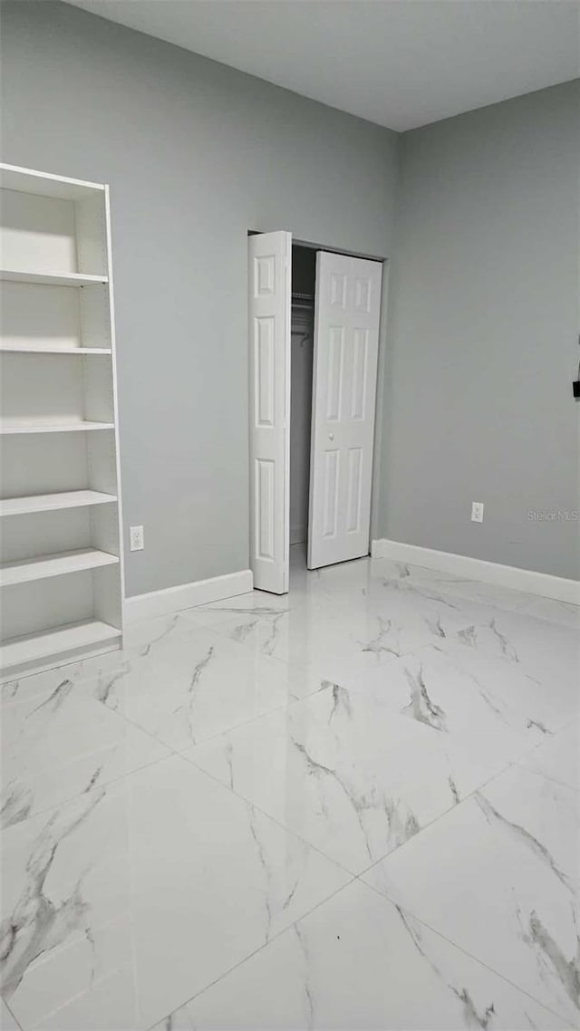 unfurnished bedroom with marble finish floor and baseboards