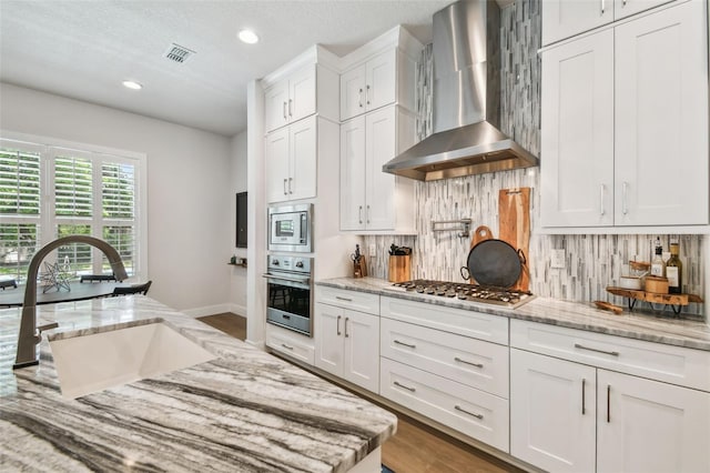 3607 W Roland St, Tampa, FL 33609 - kitchen featuring a sink, wall chimney exhaust hood, visible vents, white cabinets, and appliances with stainless steel finishes