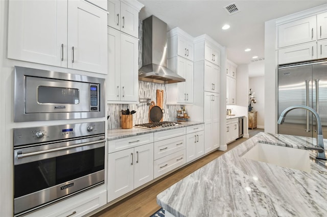 3607 W Roland St, Tampa, FL 33609 - kitchen featuring built in appliances, backsplash, a sink, white cabinetry, and wall chimney exhaust hood