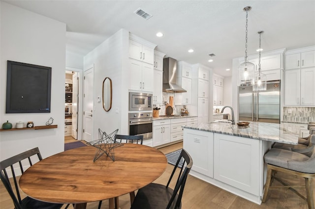 3607 W Roland St, Tampa, FL 33609 - kitchen featuring light wood-style flooring, a sink, built in appliances, visible vents, and wall chimney exhaust hood