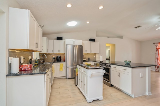 kitchen featuring a sink, appliances with stainless steel finishes, white cabinetry, backsplash, and lofted ceiling