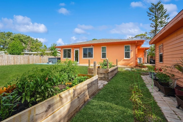 back of house with a yard, a garden, fence, and stucco siding