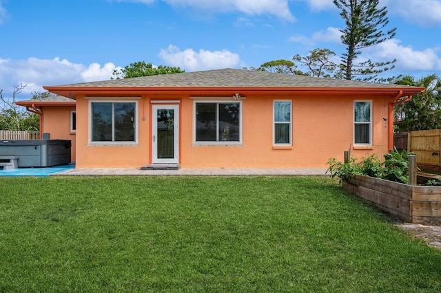 rear view of house featuring a yard, fence, stucco siding, and a hot tub