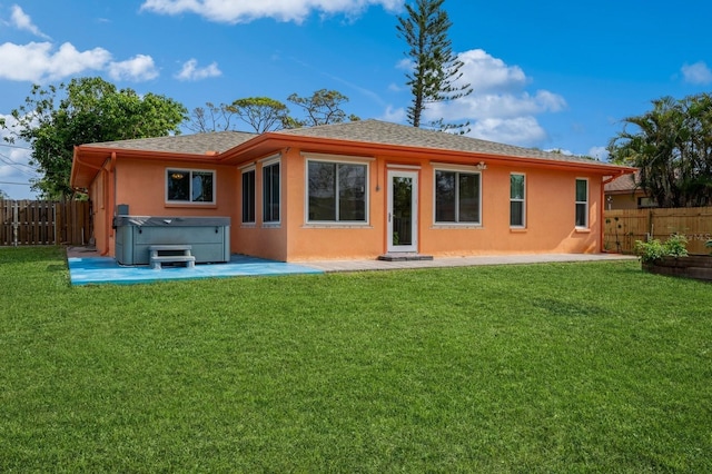 back of house featuring a hot tub, a patio area, a lawn, stucco siding, and fence private yard