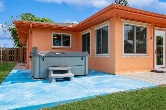 back of house featuring a patio area, stucco siding, fence, and a hot tub