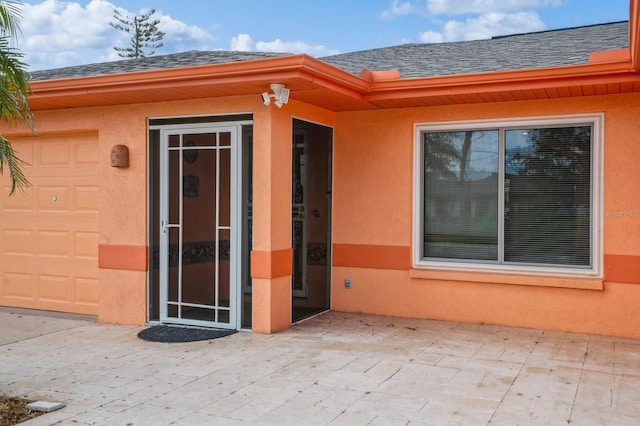 entrance to property featuring a shingled roof and stucco siding