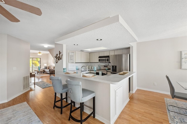 2387 Hanover Dr Unit 2387, Dunedin, FL 34698 - kitchen with stainless steel appliances, a ceiling fan, a textured ceiling, a kitchen breakfast bar, and light wood finished floors