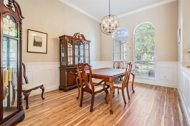 dining area featuring a decorative wall, a chandelier, crown molding, wainscoting, and light wood-style flooring