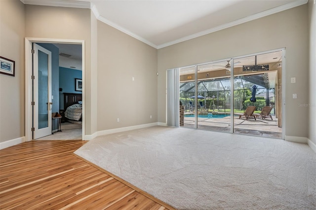 unfurnished room with baseboards, a sunroom, a ceiling fan, crown molding, and wood finished floors