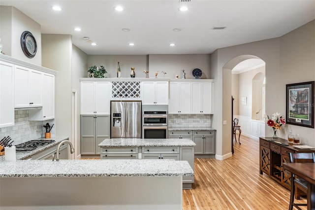 kitchen featuring tasteful backsplash, light wood-style floors, appliances with stainless steel finishes, arched walkways, and a sink