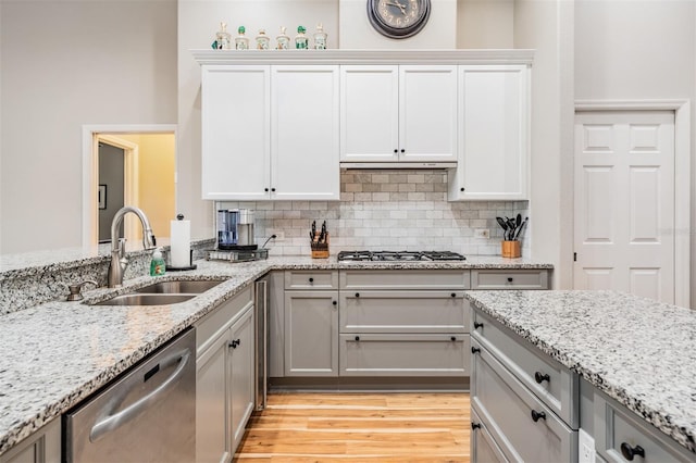 kitchen with under cabinet range hood, light stone countertops, decorative backsplash, stainless steel appliances, and a sink