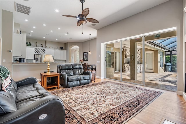 living room with light wood-type flooring, recessed lighting, visible vents, ceiling fan, and arched walkways