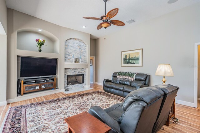 living room with baseboards, a stone fireplace, visible vents, ceiling fan, and wood finished floors