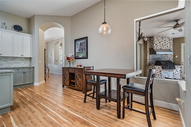 dining area featuring ceiling fan, light wood finished floors, arched walkways, and baseboards
