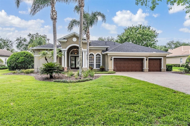 view of front facade featuring stucco siding, decorative driveway, a front lawn, an attached garage, and french doors