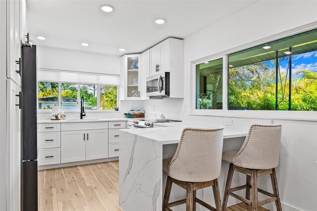 kitchen featuring stainless steel microwave, a kitchen breakfast bar, freestanding refrigerator, light stone countertops, and range with electric stovetop