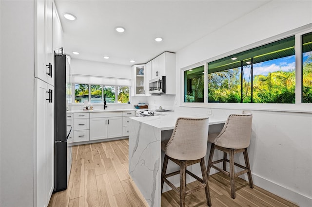 kitchen with a kitchen breakfast bar, light wood-type flooring, white cabinets, light stone countertops, and stainless steel appliances
