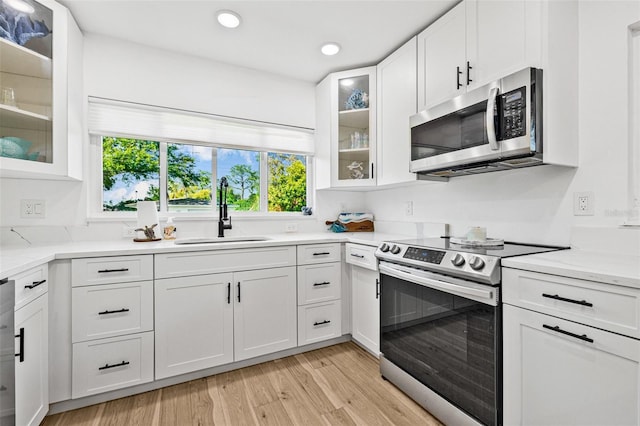 kitchen featuring glass insert cabinets, a sink, light wood-type flooring, appliances with stainless steel finishes, and white cabinetry
